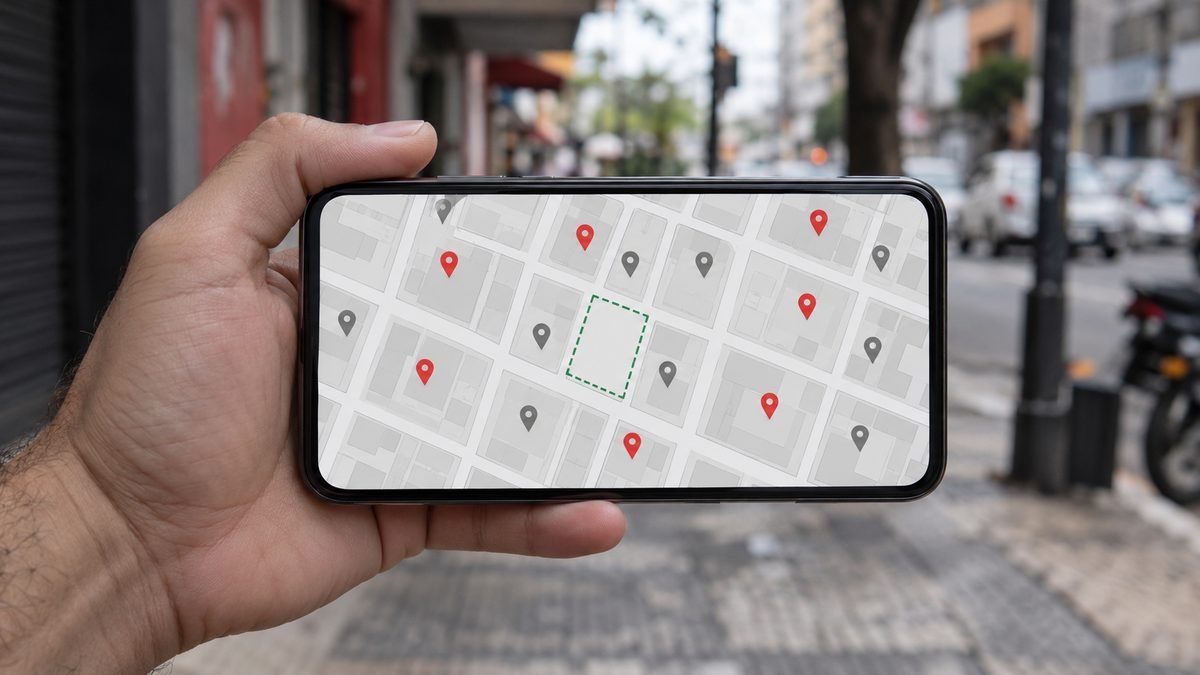 Mão segurando o celular com um mapa de bairro cheio de marcadores de outros estabelecimentos e um espaço vazio no meio